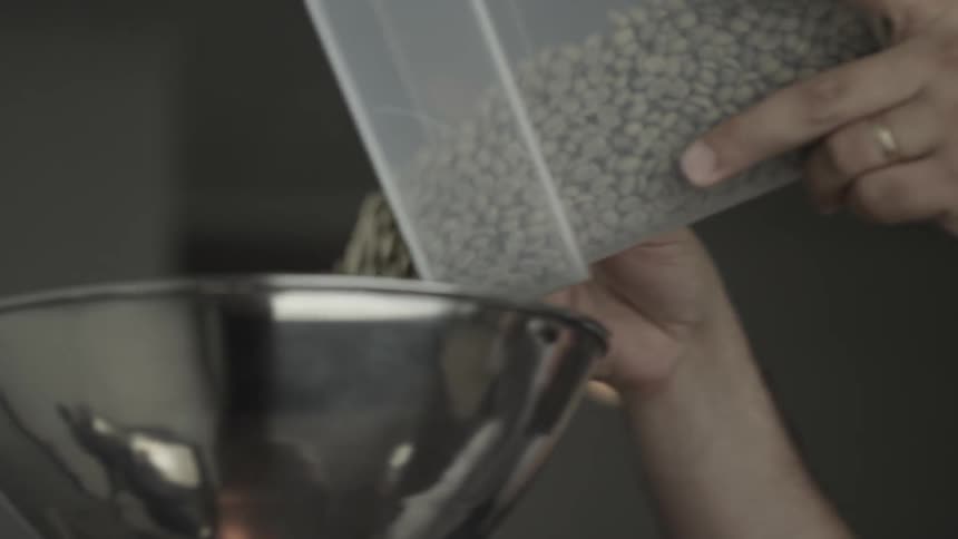 A man reaches up with a container pouring beans into a cylinder
