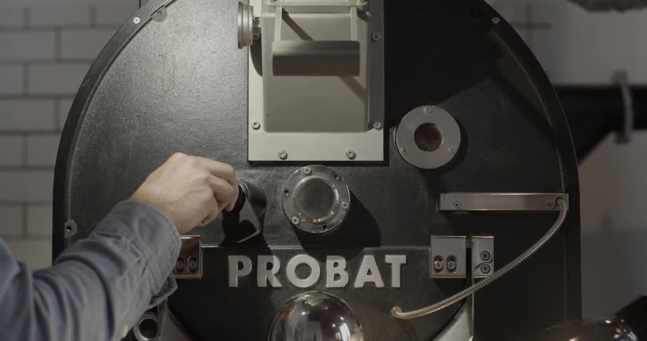 A man turns a knob and then walks away from a coffee roaster machine