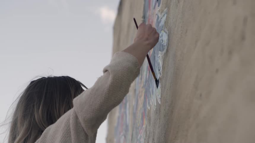 Woman paints a mural on a wall outside