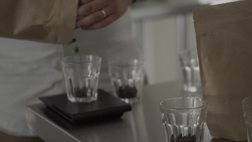 A person pours coffee beans into small glasses