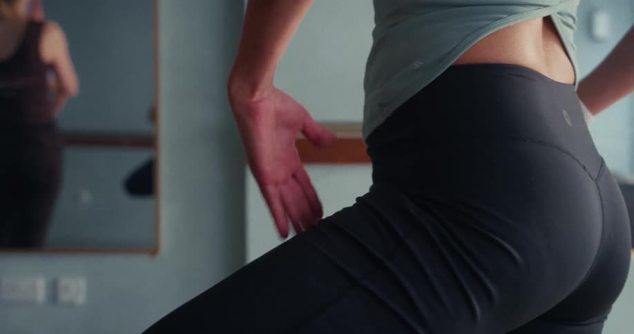 A detailed slow-motion close-up of a woman's hand and body as she holds a yoga pose in a studio