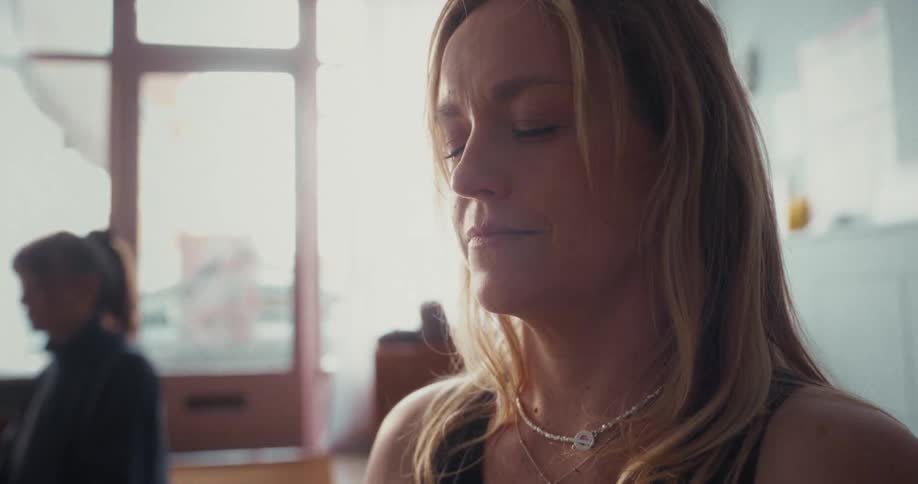 A serene blonde woman meditates with her eyes closed in a brightly lit room