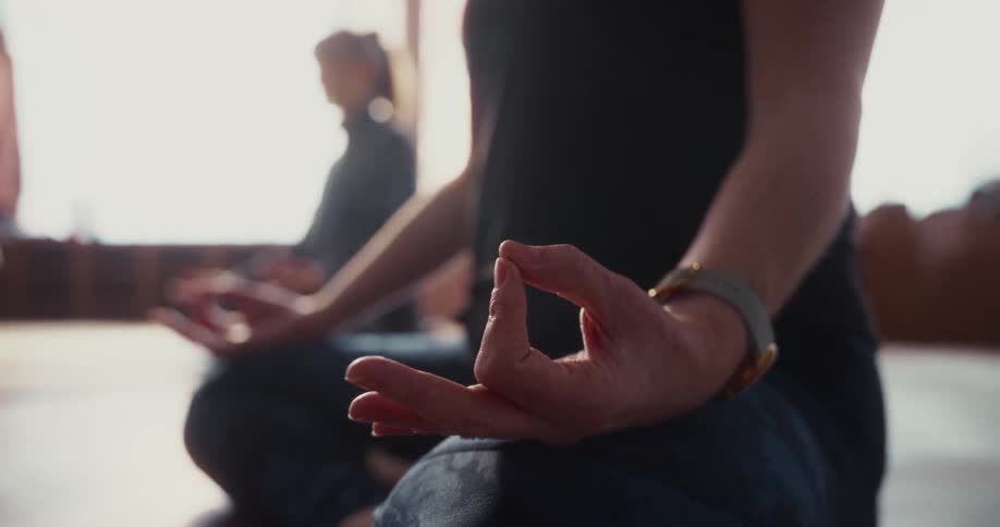 A tranquil close-up shot of a hand in a meditation pose, with soft morning light illuminating the room