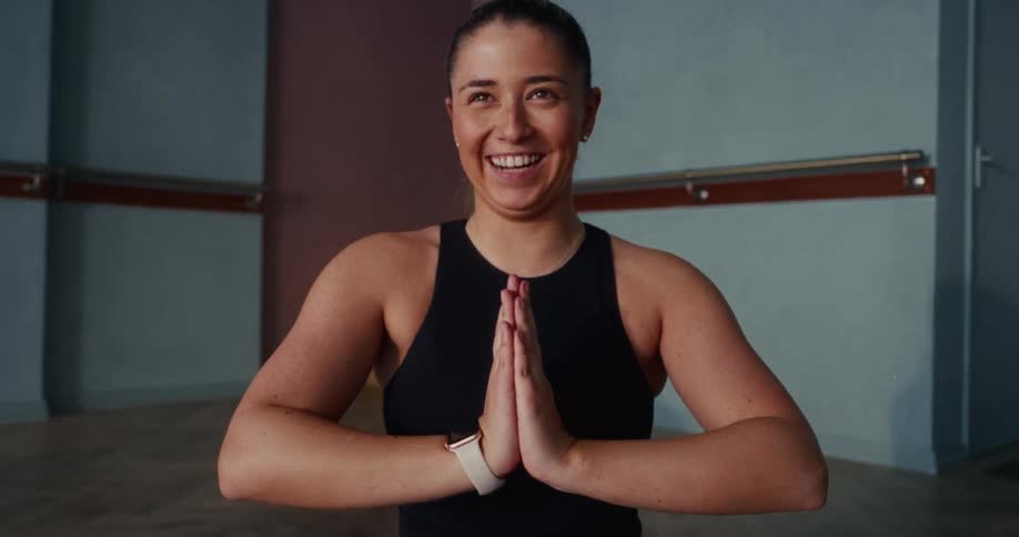 A happy woman in a yoga prayer pose smiles and then bursts into joyful laughter in a studio