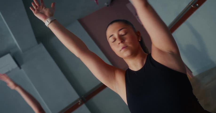 Two women gracefully perform a synchronized slow-motion yoga stretch in a dimly lit fitness studio