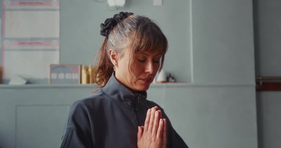 A serene woman with closed eyes meditates with her hands in a prayer position