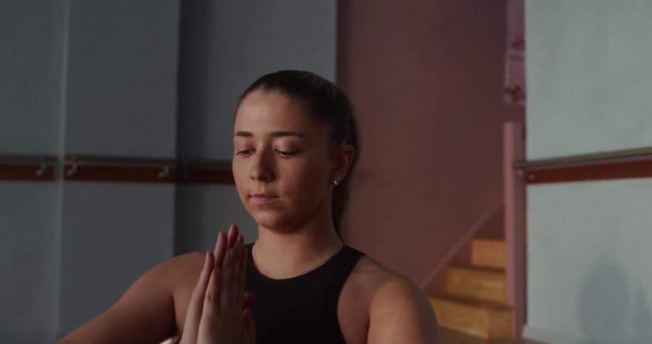 A young woman in a yoga class gracefully raises her arms and brings them into a prayer position to meditate