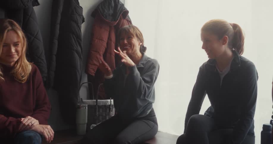 Four women friends share stories and laughter while relaxing in a locker room after a workout