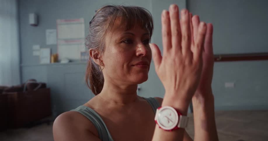 A woman centers herself, bringing her palms together in a prayer pose during a quiet yoga class