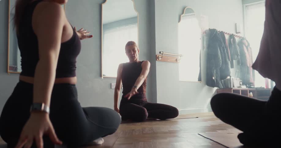 A low-angle, slow-motion shot of a yoga instructor leading her class through a seated twisting stretch in a bright studio