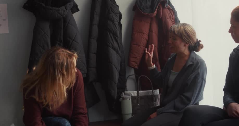 Two women friends share a funny story and laugh together in the locker room of a fitness studio