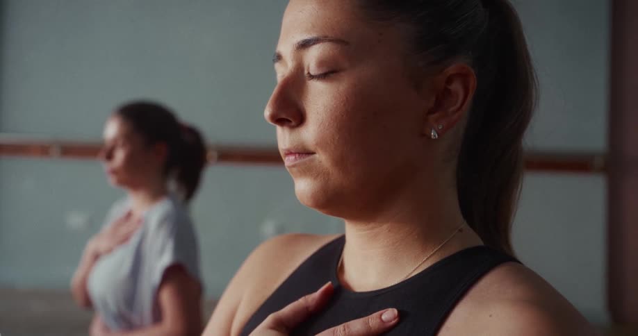 A young woman with her eyes closed meditates peacefully with her hand on her chest during a yoga class