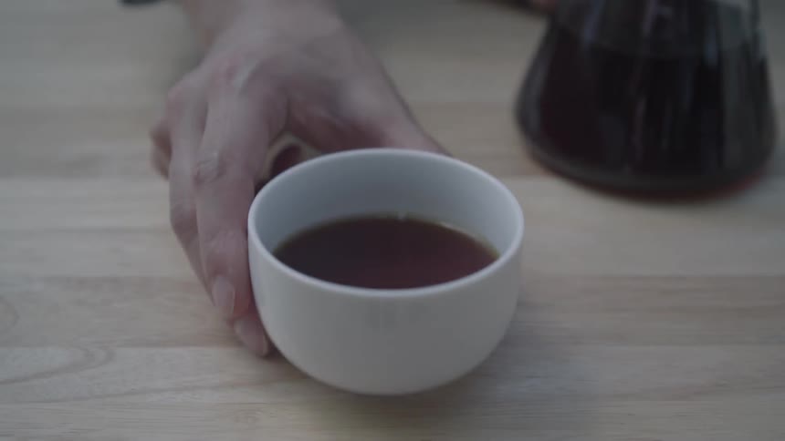 Person pushing a mug of liquid across a table