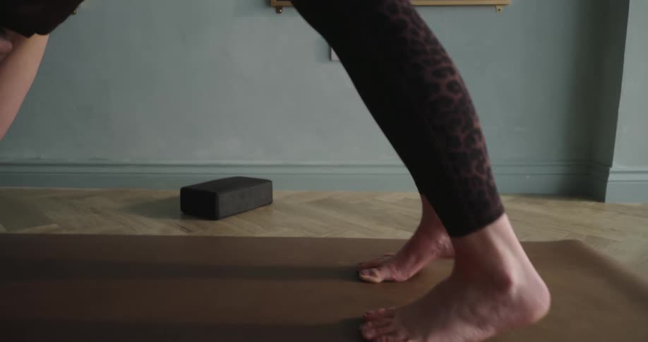Slow-motion close-up of a woman's feet and body as she transitions into the downward-facing dog yoga pose