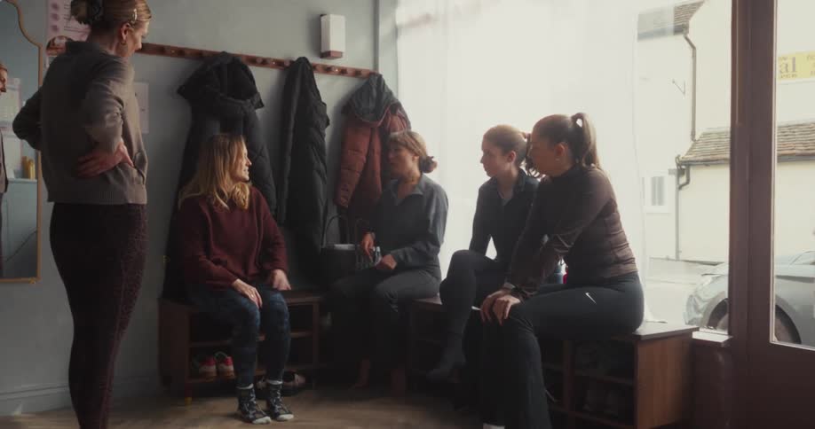 A group of women chat and get ready in the sunlit entryway of a fitness studio before a class