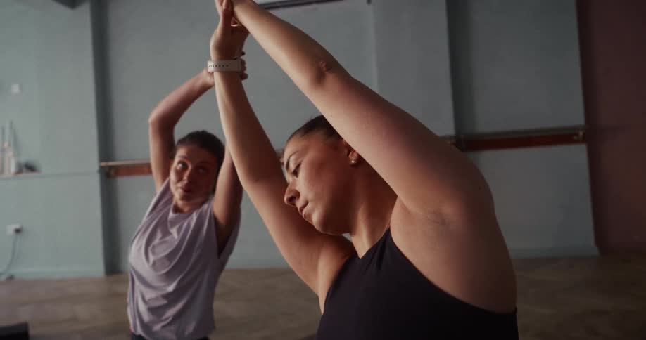 A low angle close-up of two focused women performing a side-bend stretch during a yoga class in a studio