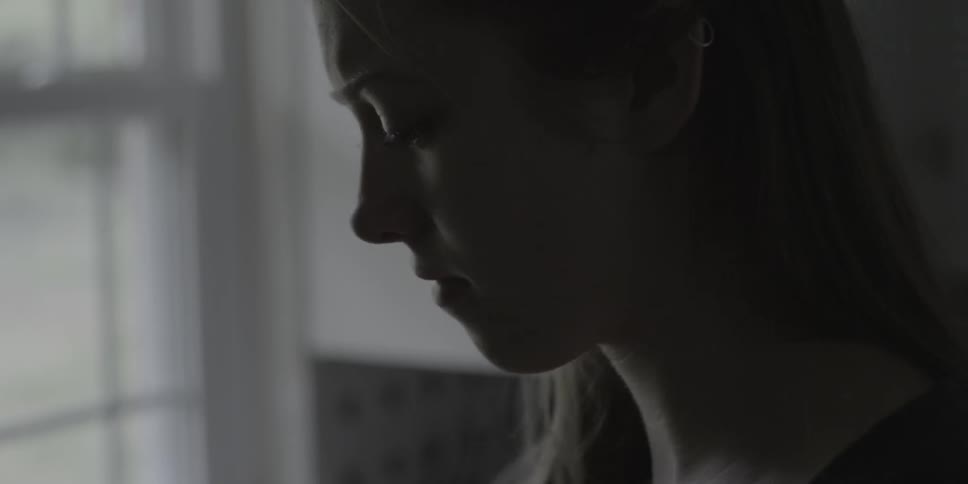 A sad looking woman stands near a window