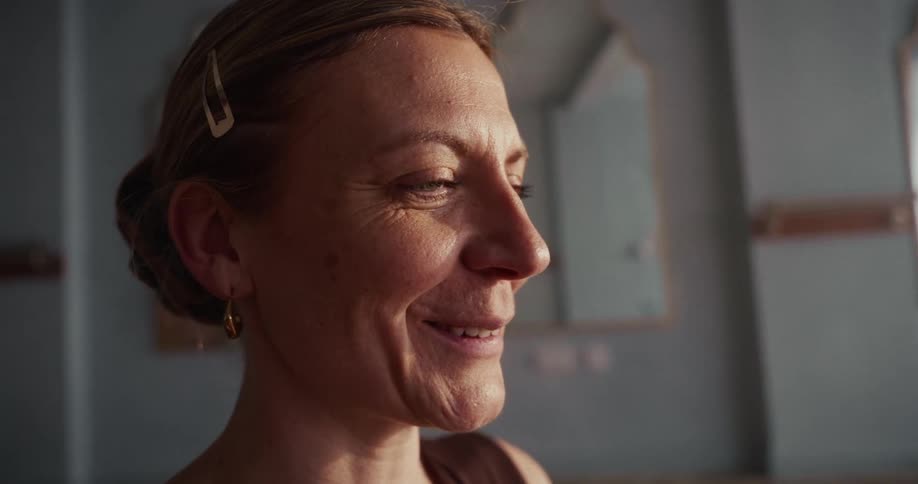A slow-motion close-up profile shot of a serene middle-aged woman breaking into a warm, genuine smile