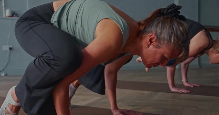 A focused woman in a yoga class holds a challenging crow pose before losing her balance in slow motion