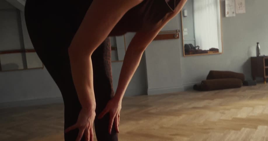 Close-up slow motion of a woman bending into a forward fold yoga pose in a tranquil studio