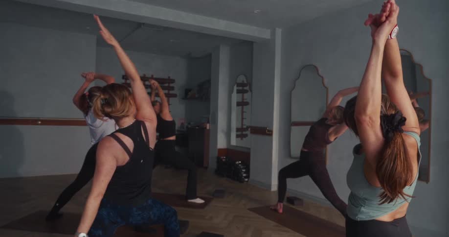 An instructor leads a yoga class of women through flowing poses in a serene, modern studio