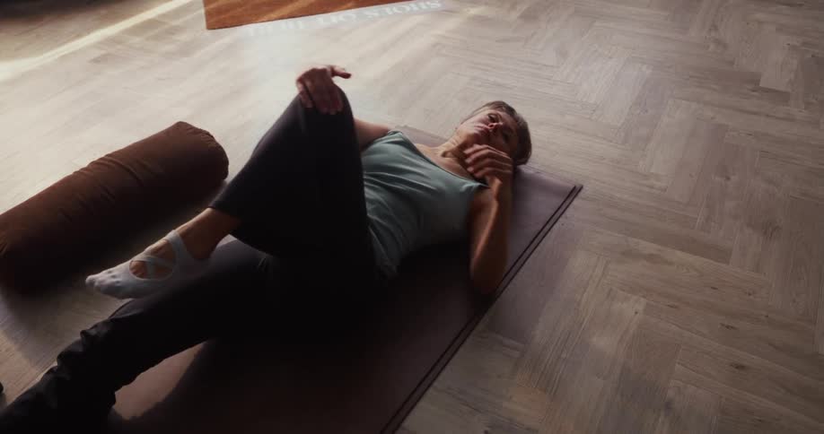 An overhead view of a woman doing gentle back stretches on a yoga mat in a calm studio
