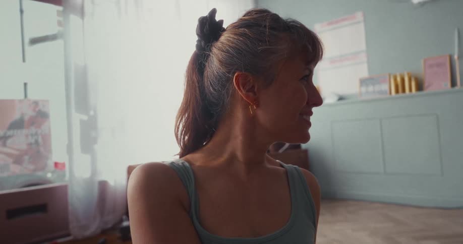 A close-up profile shot of a smiling woman with her hair in a ponytail, sitting in a softly lit room