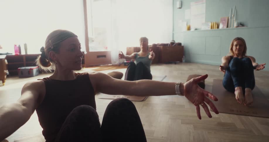 Slow-motion pull focus from feet to a woman leading a yoga class in a bright studio