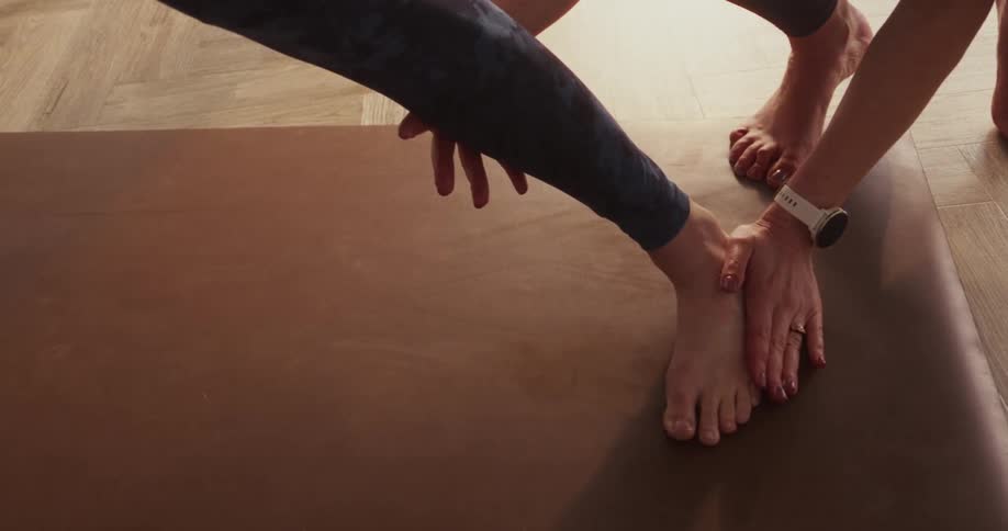 A yoga instructor provides hands-on assistance to a student, adjusting their foot alignment in a lunge pose during a class