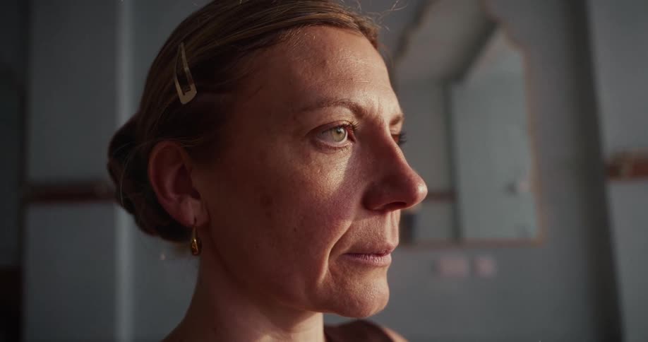 A thoughtful middle-aged woman slowly opens her eyes in a quiet, sunlit room, emerging from a moment of reflection