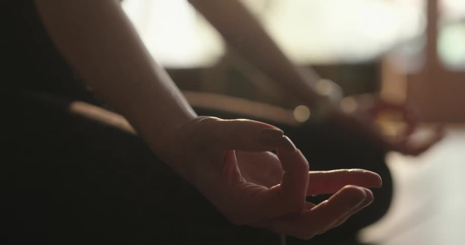 Sunlight illuminates a person's hand held in a mudra pose during a calm meditation session