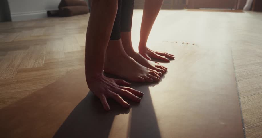 A close-up shot of a person's bare feet and hands stretching on a yoga mat in the warm sunlight