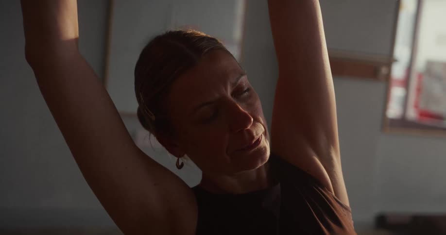 Close up of a serene woman in a sunlit room closing her eyes while doing a deep yoga side stretch