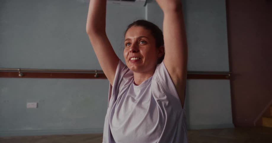Close-up slow-motion shot of a smiling woman gently stretching her arms and torso in a yoga studio
