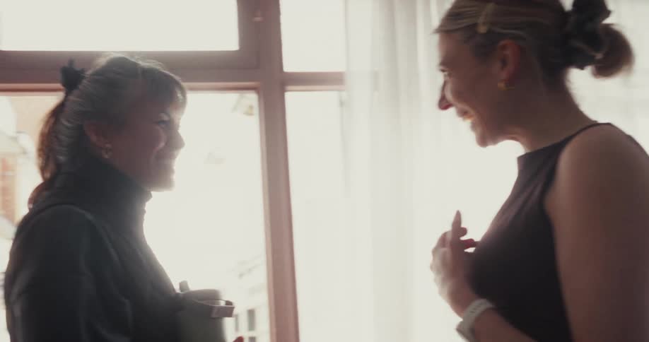 An older woman and a younger woman share a loving embrace and then have a joyful conversation by a bright window