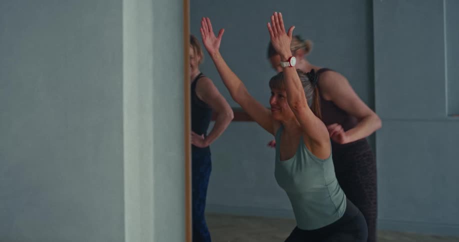 A yoga instructor provides gentle, hands-on assistance to a smiling student perfecting her pose in a fitness studio