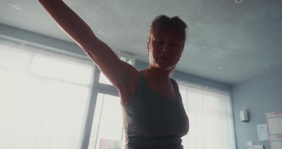 Slow motion close up of a focused woman gracefully transitioning through yoga poses in a bright, sunlit room