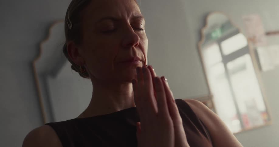 Low-angle close-up of a serene woman meditating with her eyes closed and hands held together in a prayer pose