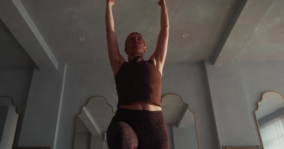 A woman gracefully performs a crescent lunge yoga pose in slow motion, showcasing strength and balance from a low angle perspective