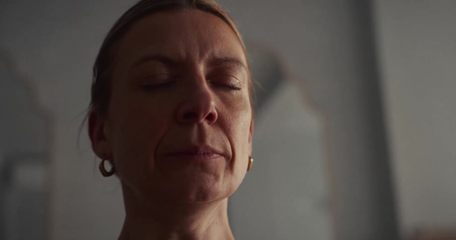 A serene middle-aged woman finds a moment of calm, meditating with her eyes closed in a softly lit room
