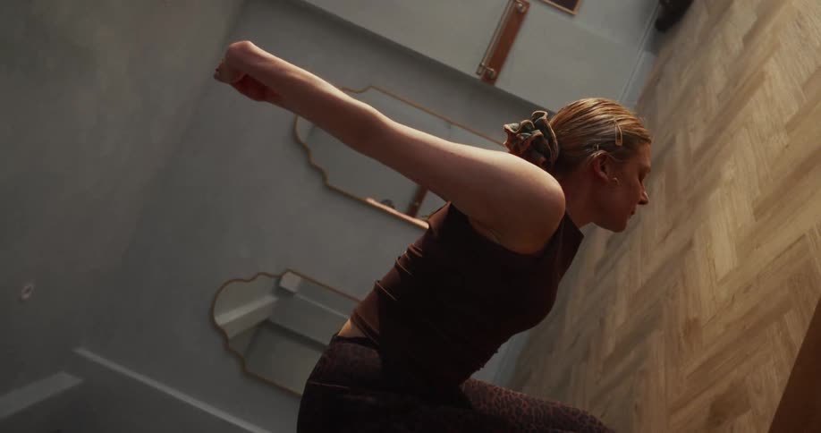 A focused woman holds a deep seated forward bend yoga pose in a tranquil studio, shot in slow motion with a unique rotating perspective