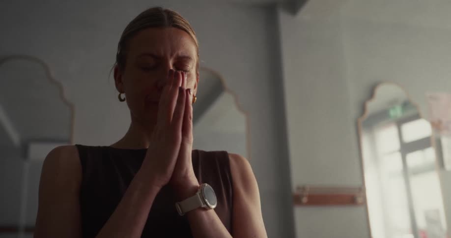A peaceful woman with her eyes closed meditates with her hands together in a prayer position
