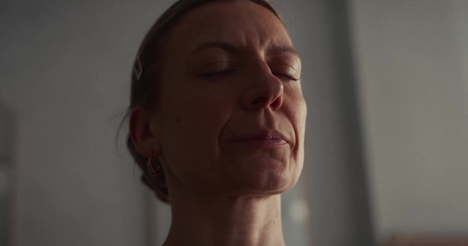 A serene middle-aged woman with her eyes closed finds a moment of peace and tranquility while meditating