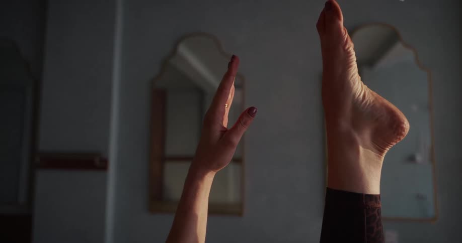 A woman's hand and foot are held up in the air as she performs a relaxing yoga stretch in a softly lit room