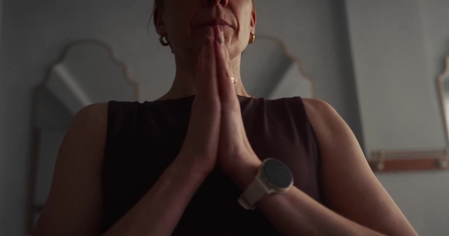A serene woman with closed eyes meditates with her hands together in a prayer position during a moment of mindfulness