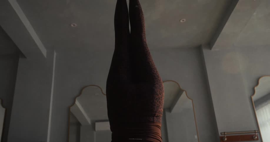 A slow vertical pan reveals a woman holding a perfect yoga headstand in a tranquil studio