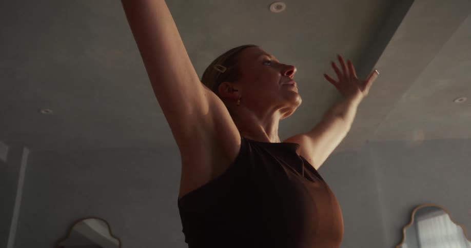 Graceful woman performs a fluid sun salutation yoga sequence in a sunlit studio in slow motion