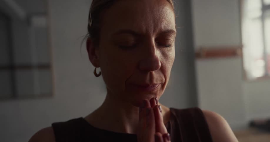A tranquil woman meditates with closed eyes and hands in a prayer pose, finding a moment of peaceful mindfulness