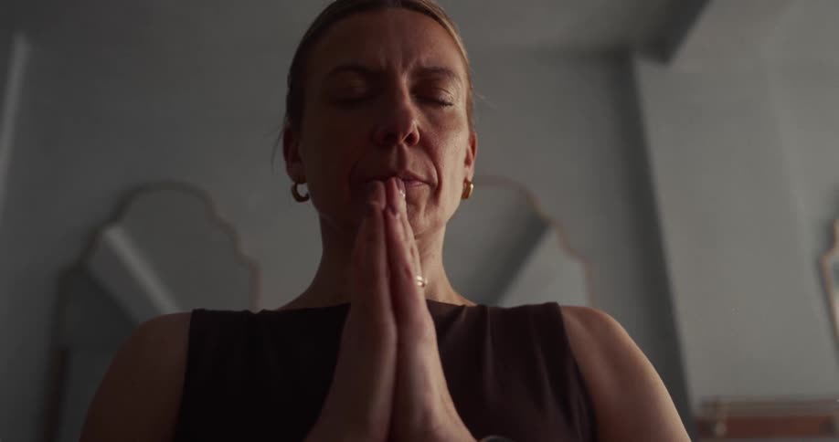 A serene woman with closed eyes brings her hands together in a prayer pose, finding tranquility during her meditation practice