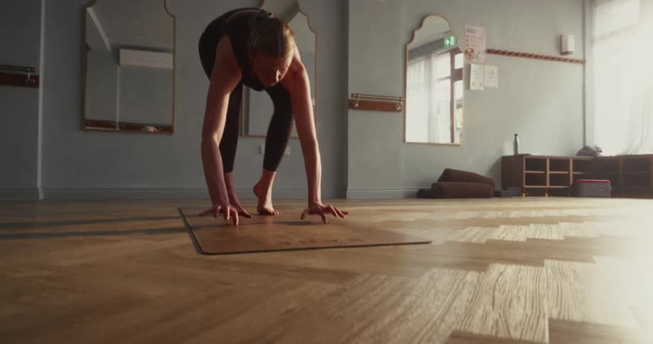 A strong woman gracefully executes a challenging arm balance yoga pose in slow motion within a beautifully lit studio